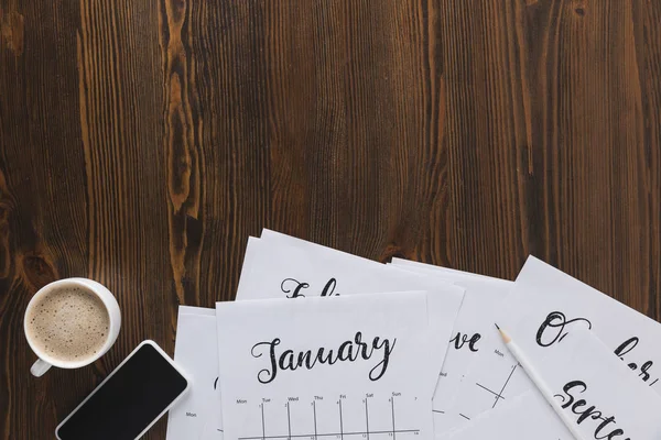 Pose plate avec des papiers calendrier en papier, smartphone et tasse de café sur table en bois — Photo de stock