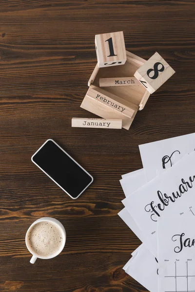Vue de dessus du smartphone arrangé, tasse de café, pièces de calendrier sur la surface en bois — Photo de stock