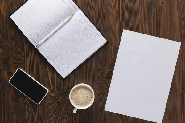 Posa piatta con smartphone, notebook, matita e tazza di caffè su tavolo in legno — Foto stock