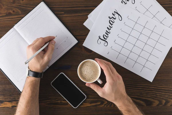 Vista parcial del hombre de negocios tomando notas en cuaderno en la mesa con calendario - foto de stock