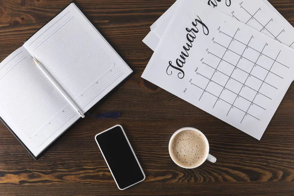 Piso con cuaderno vacío, calendario, lápiz y teléfono inteligente en la superficie de madera - foto de stock