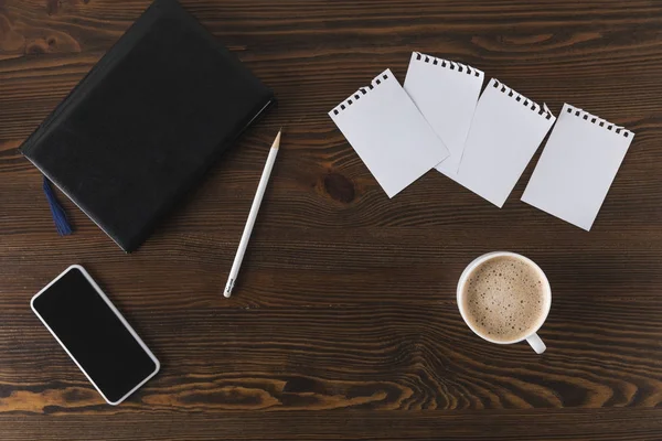 Flat lay with smartphone, notebook, pencil and cup of coffee on wooden tabletop — Stock Photo