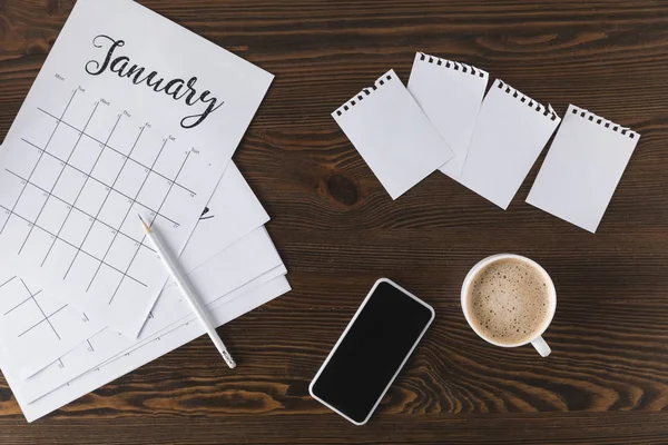 Piso con cuaderno vacío, calendario, lápiz y teléfono inteligente en la superficie de madera - foto de stock