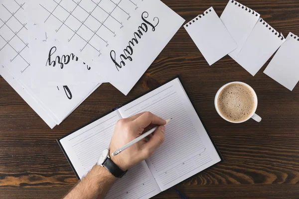 Partial view of businessman making notes in notebook at table with calendar — Stock Photo