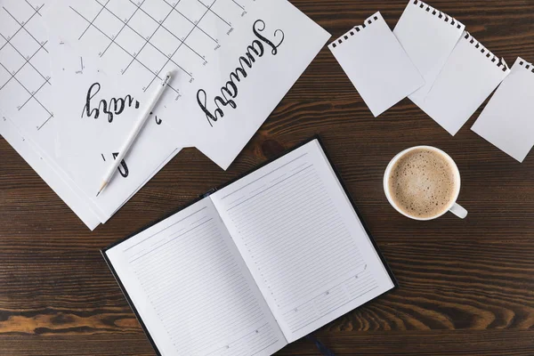 Flat lay with empty notebook, calendar and cup of coffee on wooden surface — Stock Photo