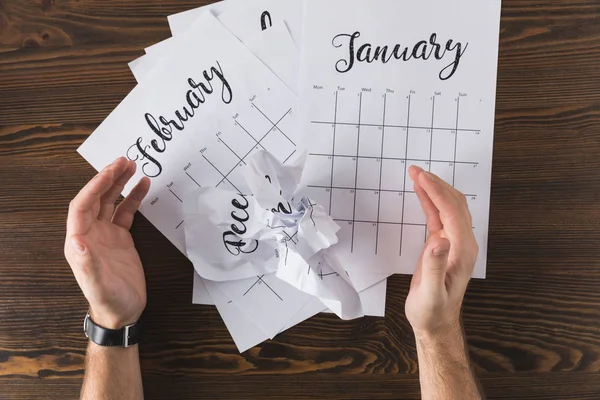 Abgeschnittene Aufnahme männlicher Hände und zerrissener Kalender auf hölzerner Tischplatte — Stockfoto