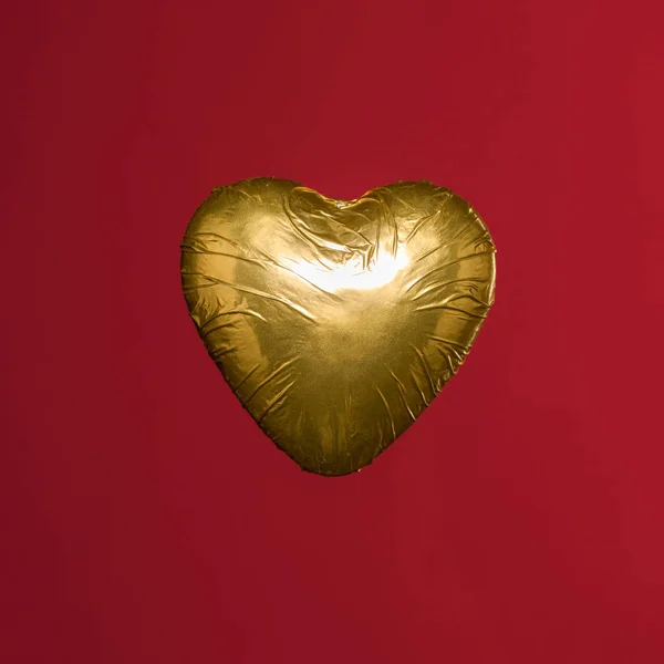 Heart shaped candy in golden wrapper isolated on red — Stock Photo