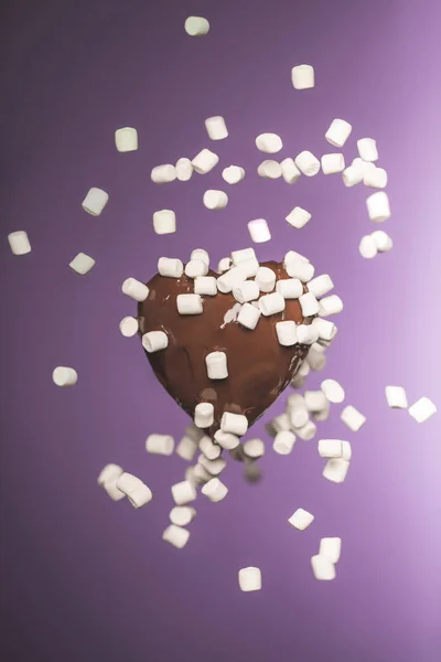 Heart shaped chocolate candy with falling marshmallow isolated on purple — Stock Photo
