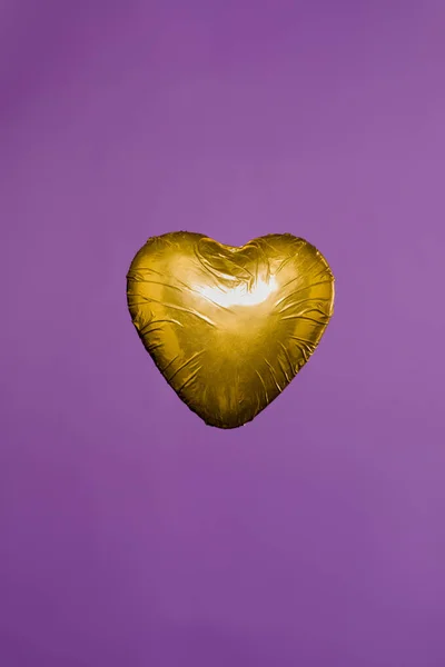 Caramelle a forma di cuore in involucro dorato isolato su viola — Foto stock