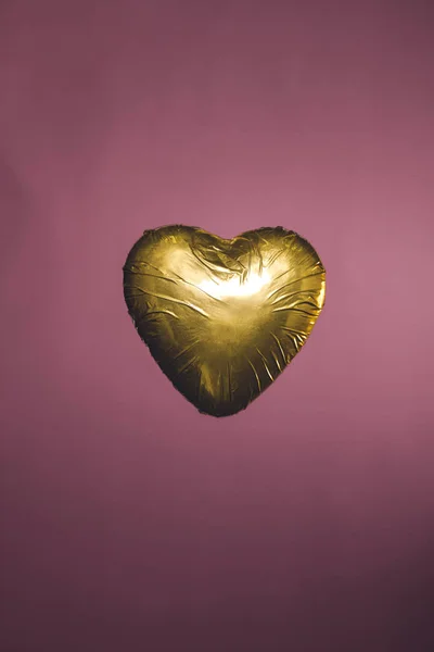 Heart shaped candy in golden wrapper isolated on pink — Stock Photo