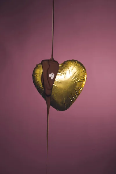 Caramelo en forma de corazón en una envoltura dorada con chocolate líquido vertido aislado en rosa - foto de stock