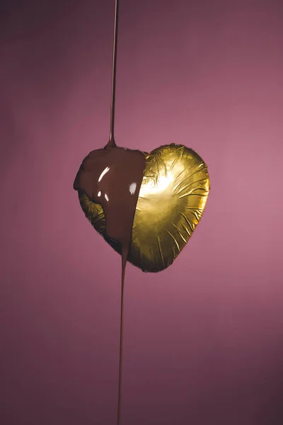 Конфеты в форме сердца в золотой обертке с жидким шоколадом изолированы на розовый — стоковое фото