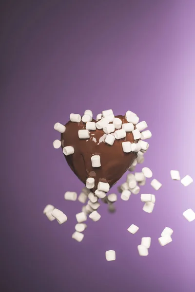 Chocolate heart shaped candy with falling marshmallow isolated on purple — Stock Photo