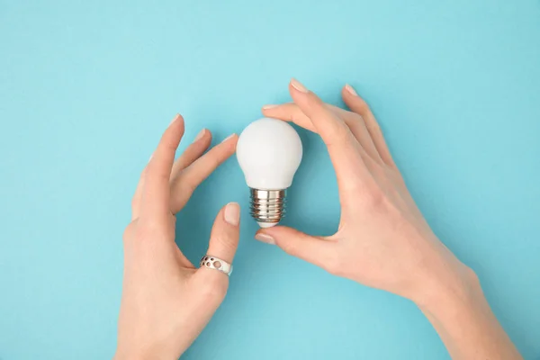 Partial view of woman holding light bulb in hands isolated on blue — Stock Photo