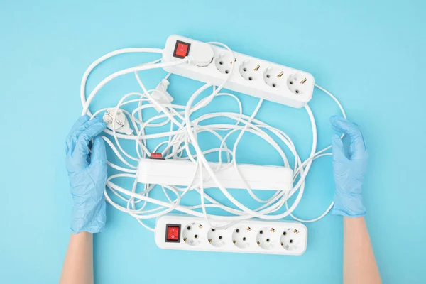 Vista parcial de las manos femeninas con guantes protectores y cordones de extensión aislados en azul - foto de stock