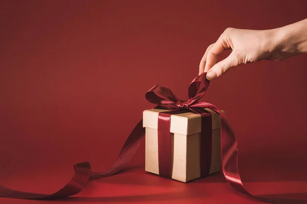 Partial view of woman holding ribbon on gift box on red — Stock Photo