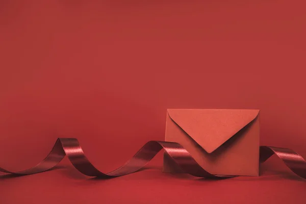 Close up view of envelope and ribbon isolated on red — Stock Photo