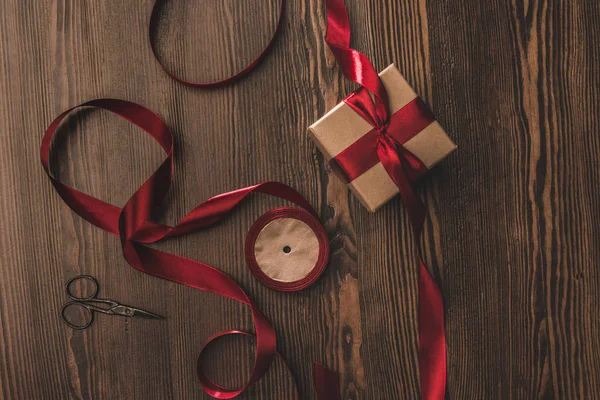Flat lay with arranged red ribbon, present and scissors on wooden surface — Stock Photo