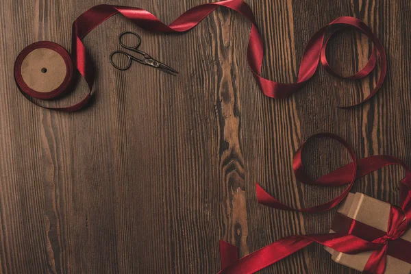 Pose plate avec ruban rouge disposé, présent et ciseaux sur la surface en bois — Photo de stock