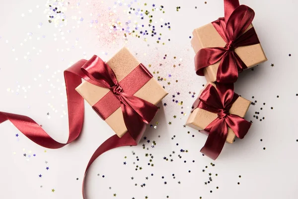 Top view of arranged gifts with red ribbons and confetti isolated on white — Stock Photo