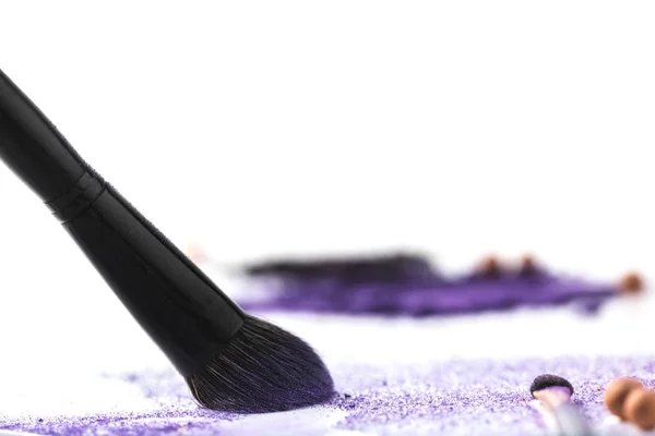 Makeup brush picking up purple cosmetic eye shadows on white surface — Stock Photo