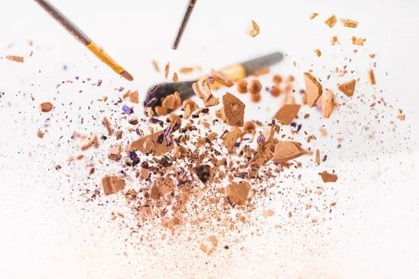 Close-up shot of pieces of cosmetic powder with makeup brushes falling isolated on white — Stock Photo