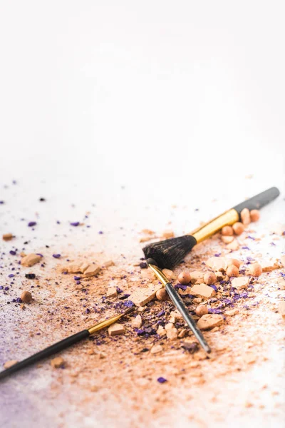 Makeup brushes lying on white surface spilled with cosmetic powder — Stock Photo