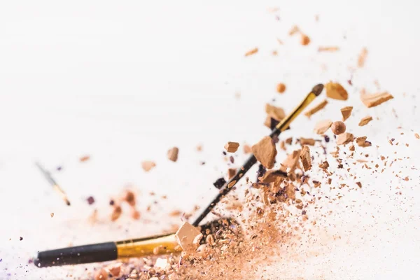 Morceaux de poudre cosmétique avec pinceaux de maquillage tombant isolés sur blanc — Photo de stock