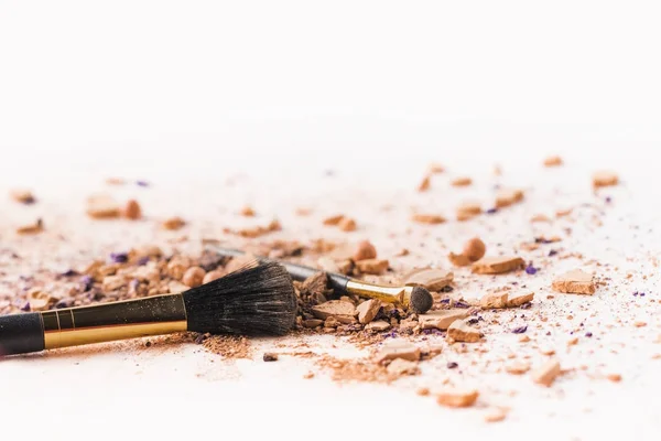 Pinceaux de maquillage couchés sur une surface blanche avec de la poudre cosmétique — Photo de stock