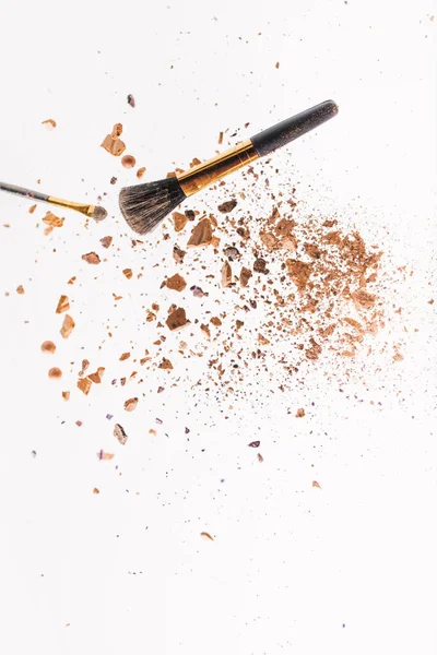 Morceaux de poudre avec pinceaux de maquillage tombant isolés sur blanc — Photo de stock