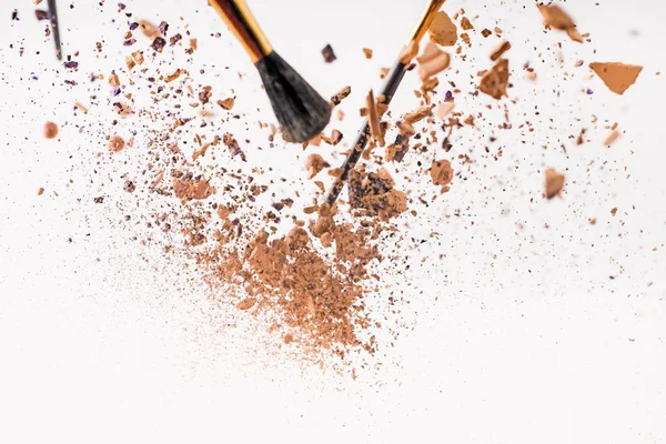 Pieces of cosmetic powder with brushes falling isolated on white — Stock Photo