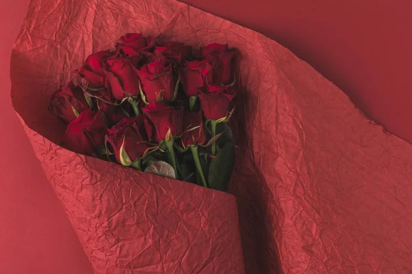 Top view of bouquet of roses in wrapping paper isolated on red — Stock Photo