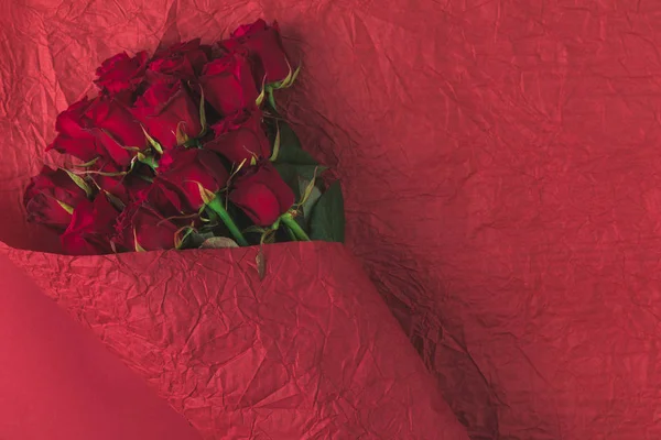 Top view of bouquet of roses in wrapping paper isolated on red — Stock Photo