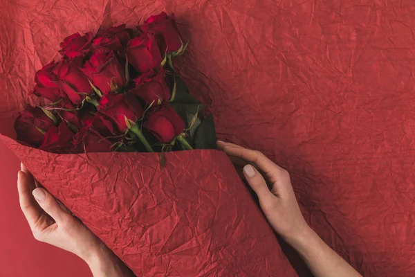 Vue partielle de la femme tenant un bouquet de roses rouges dans du papier d'emballage pour la Saint-Valentin — Photo de stock