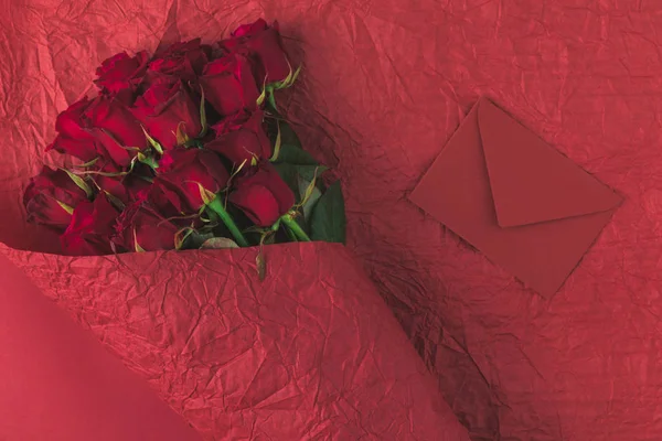 Верхний вид букета роз в оберточной бумаге и конверт изолированы на красный, день святого Валентина концепции — стоковое фото