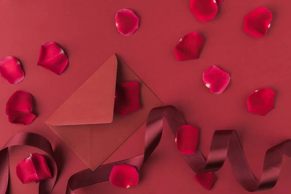 Flat lay with arranged red roses petals, envelope and ribbon isolated on red, st valentines day concept — Stock Photo