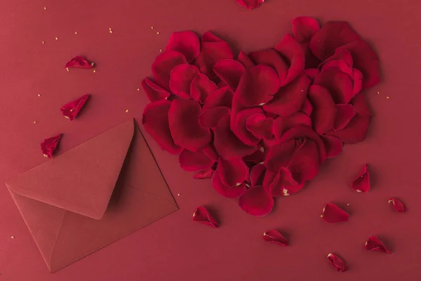 Vista dall'alto del cuore fatto di petali di rose e busta isolata su rosso, concetto giorno st valentines — Foto stock