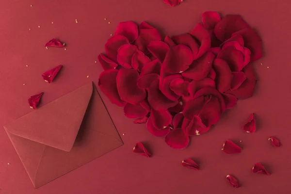 Top view of heart made of roses petals and envelope isolated on red, st valentines day concept — Stock Photo