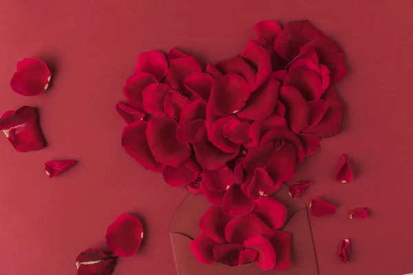 Vista superior del corazón hecha de pétalos de rosas y sobre aislado en rojo - foto de stock