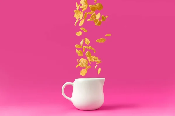 Primo piano vista di fiocchi di mais biologici che cadono in brocca di latte isolato su rosa — Foto stock