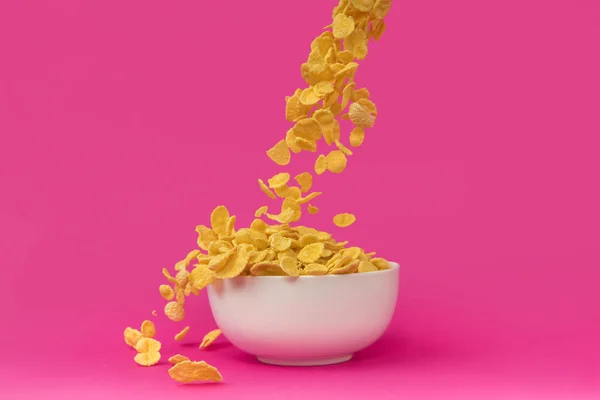 Nahaufnahme von süßen knusprigen Cornflakes, die in eine weiße Schüssel fallen, isoliert auf rosa — Stockfoto