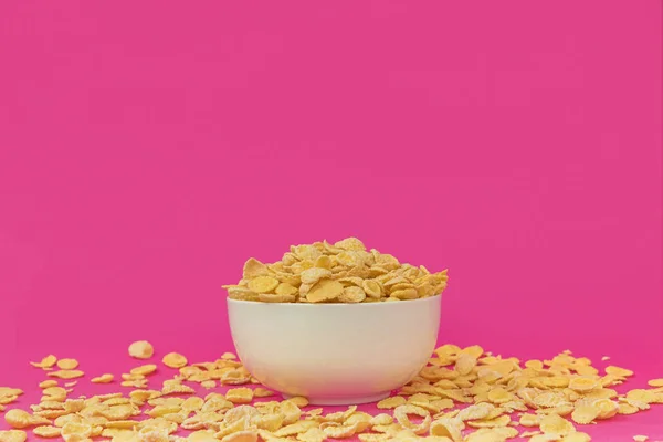 Vista de cerca del tazón blanco y deliciosos copos de maíz crujientes en rosa - foto de stock