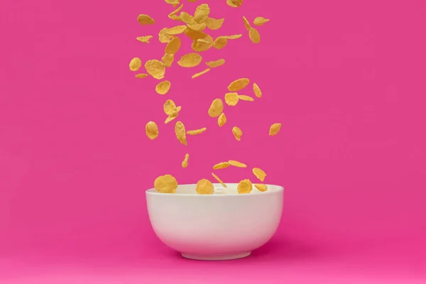 Vista close-up de deliciosos flocos de milho caindo em tigela branca isolada em rosa — Fotografia de Stock