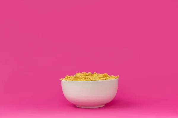 Nahaufnahme der weißen Schüssel mit gesunden, knusprigen Cornflakes isoliert auf rosa — Stockfoto