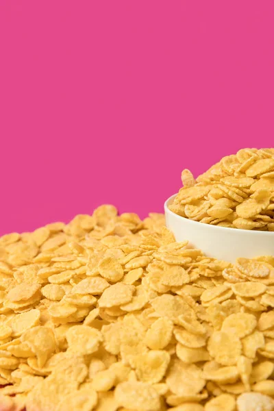 Close-up view of fresh crunchy corn flakes and white bowl isolated on pink — Stock Photo