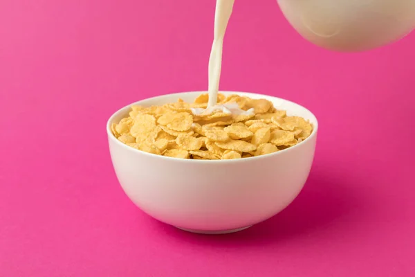 Nahaufnahme von Milch gießt in Schüssel mit Cornflakes isoliert auf rosa — Stockfoto