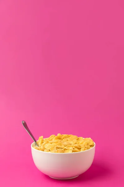 Gesundes Frühstück mit leckeren Cornflakes und Milch in Schüssel mit Löffel isoliert auf rosa — Stockfoto