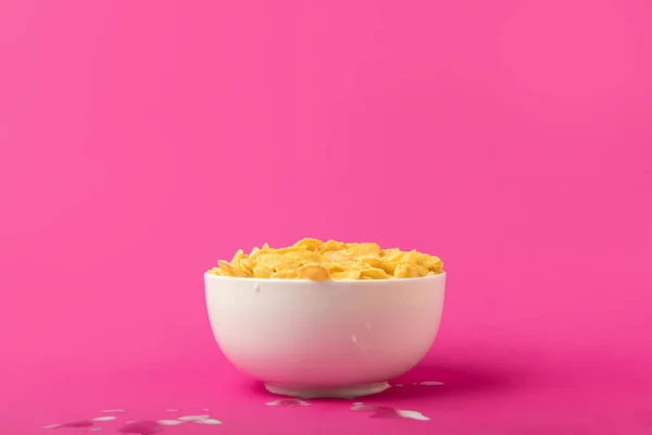 Colazione sana con gustosi corn flakes e latte in ciotola isolato su rosa — Foto stock