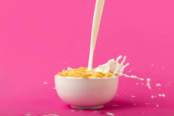 Vista de cerca de verter leche orgánica fresca en un tazón con hojuelas de maíz en rosa - foto de stock