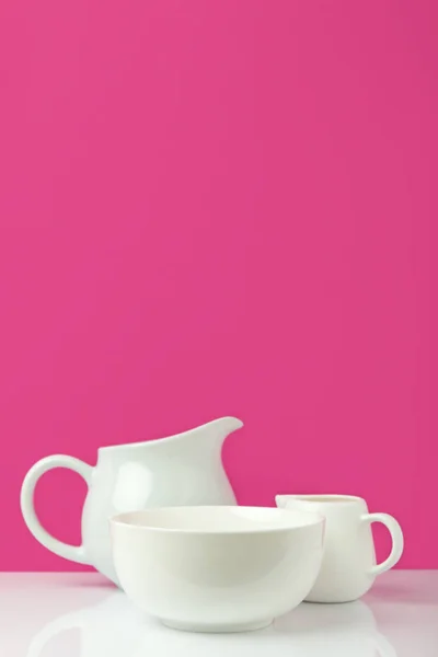 Vista ravvicinata di ciotola bianca vuota, brocca grande e brocca di latte su rosa — Foto stock